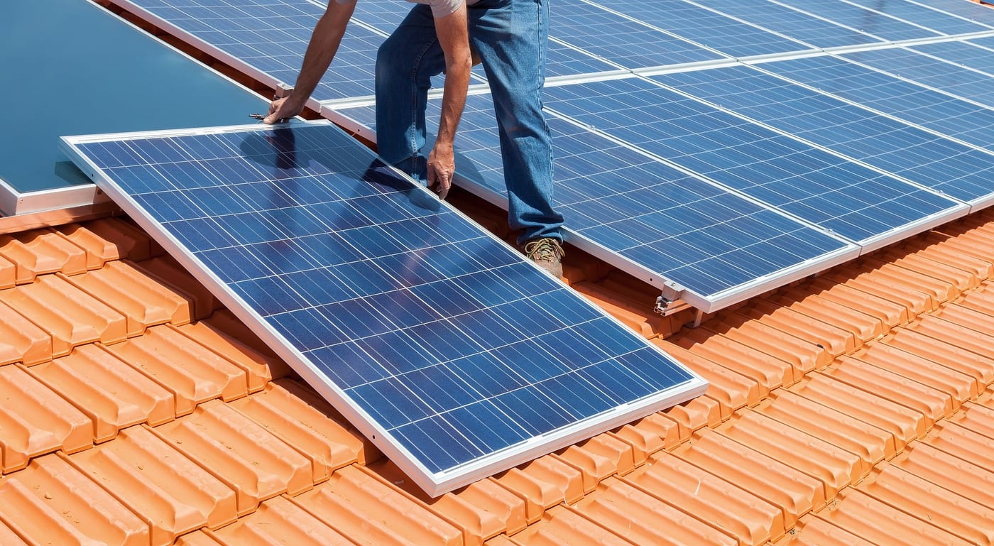 Solarteur setzt ein Solarmodul auf die Montageschiene eines Ziegeldachs