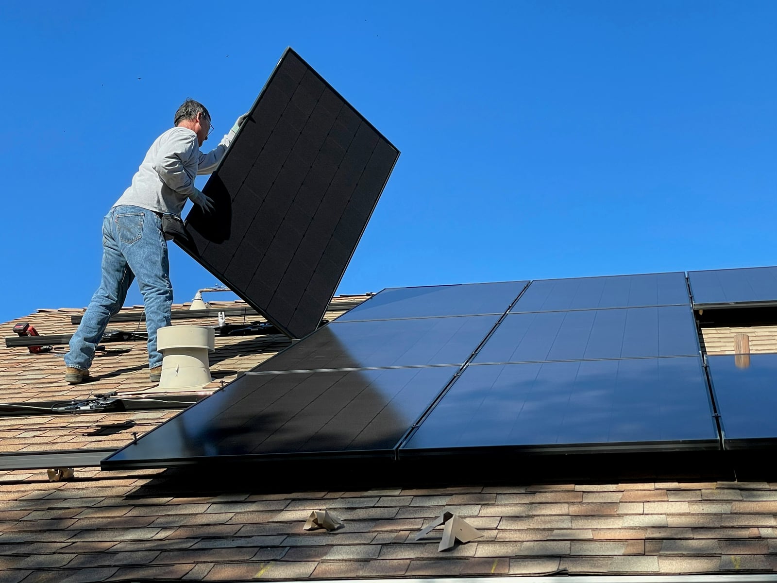 Solarteur montiert ein Solarmodul auf einem Ziegeldach vor blauem Himmel