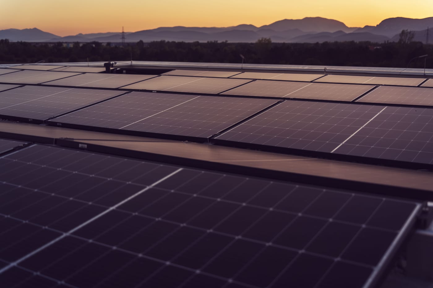 Vom Solarteur aufgeständerte Photovoltaikanlage auf einem Flachdach im Abendlicht mit Strommast im Hintergrund