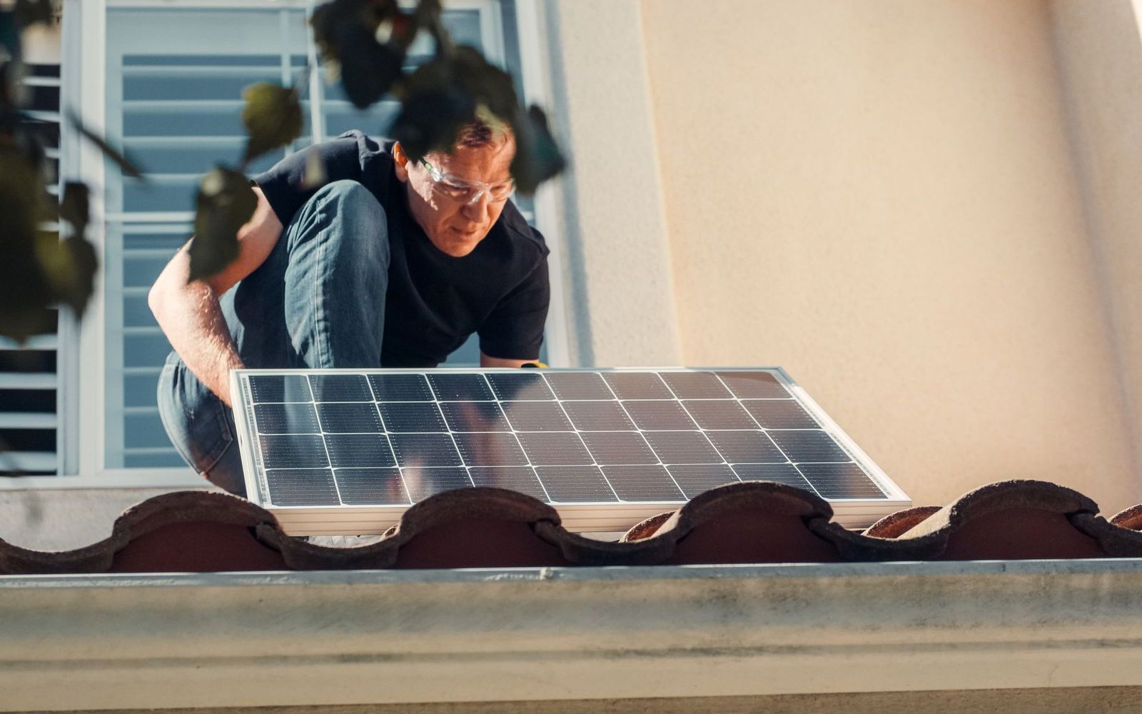 Solarteur kniet auf einem Ziegeldach und setzt ein Solarmodul am Dachrand an