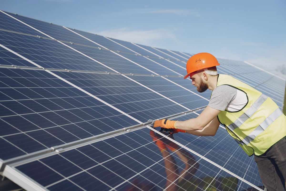 Solarteur mit orangem Helm justiert ein Solarmodul in der Modulreihe