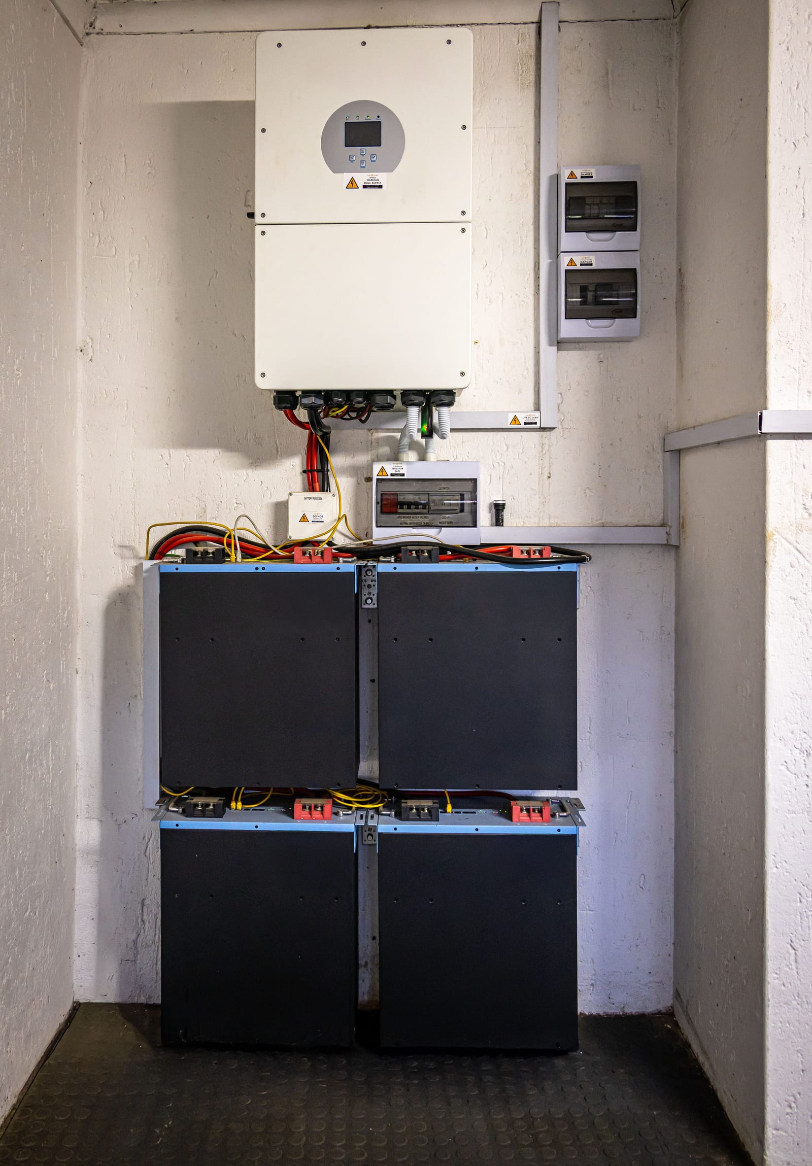Vom Solarteur angeschlossener Wechselrichter mit darunter aufgereihten Batteriemodulen in einem Technikraum